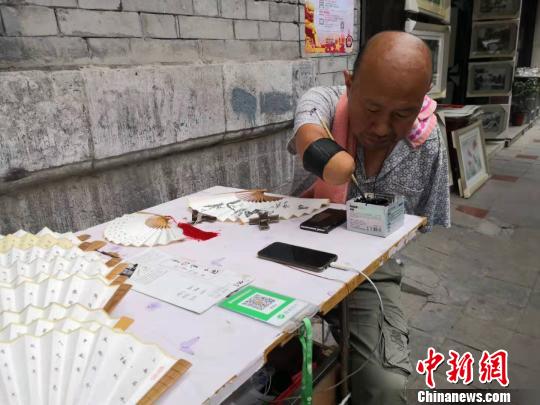 賈維軍坐在自己的簡易攤位前寫字,。　阿琳娜 攝