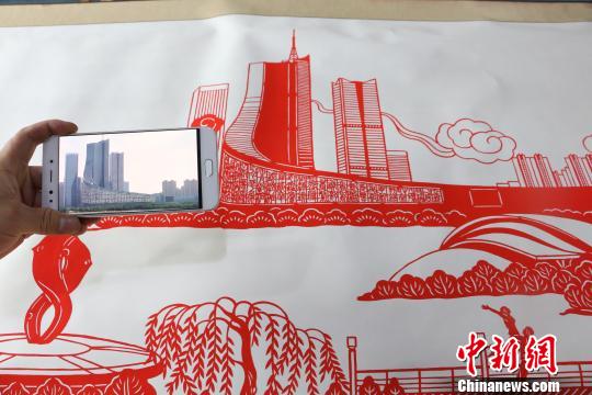 圖為丁健對比照片與剪紙作品,。　夏瑩 攝