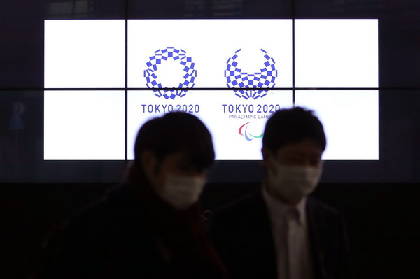 3月30日,，在日本東京新橋，行人經(jīng)過顯示東京奧運(yùn)會和殘奧會會徽的電子屏,。